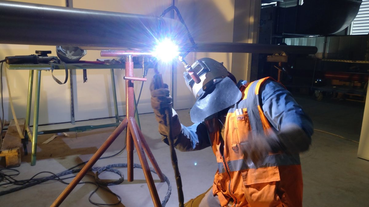 Lasser in hi-vis vest last een leidingframe op locatie